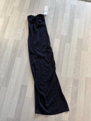Mörkblå  axelbandslös långklänning - Snygg mörkblå långklänning i ribbat material med twistad detalj framtill. Klänningen är axelbandslös och har en smickrande, figurnära passform som ger en elegant siluett. Perfekt för dig som vill sticka ut med en stilren look. Oanvänd 