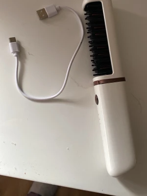 Vit bärbar värmeborste - Säljer en vit elektrisk bärbar värmeborste Borsten har tre värmeinställningar (160°C, 170°C, 180°C) och kommer med en USB-laddningskabel. Perfekt för att snabbt styla håret och få det slätt.