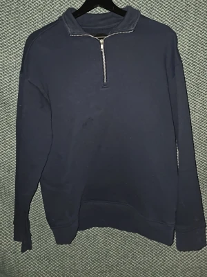 Mörkblå halvzip tröja - Mörkblå sweatshirt med halv dragkedja och hög krage. Tröjan har långa ärmar och ribbade muddar vid ärmslut och nederkant. Perfekt för lager på lager och enkel att matcha med jeans eller byxor.