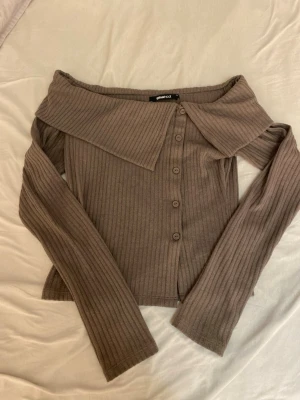 Brun ribbad off shoulder kofta Gina Tricot - Trendig brun ribbad kofta från Gina Tricot med off shoulder-design och stora krage. Knäppning framtill med fem knappar och långa ärmar. Perfekt för dig som gillar en stilren men ändå unik look.