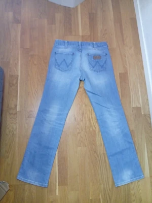 Ljusblå raka jeans med vintage-look - Säljer ett par ljusblå jeans med raka ben och klassisk femficksmodell. Jeansen har snygga slitningar och tvättade detaljer för en vintage-känsla. Materialet är denim i bomull och bakfickorna har dekorativa sömmar. Passar både S och M.