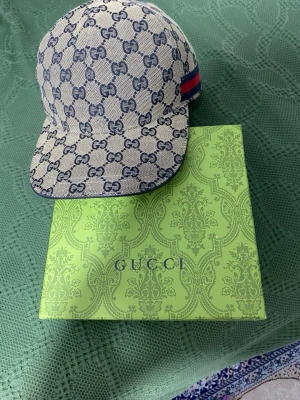 Gucci GG Supreme keps beige/blå - Säljer en snygg Gucci keps i beige med blått GG Supreme-mönster och klassisk röd-blå rand på sidan. Kepsen har justerbar rem bak och är fodrad med marinblått tyg. Materialet är canvas och kepsen kommer med original Gucci-förpackning.