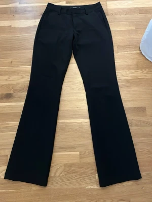 Svarta kostymbyxor från BikBok - Snygga svarta kostymbyxor från BikBok med utsvängda ben och klassisk passform. Byxorna har hällor för skärp och diskreta fickor. Perfekta för en stilren look och passar till många olika outfits.