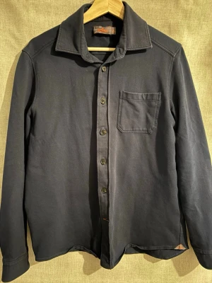 Mörkblå overshirt från morris - Stilren mörkblå over shirt från Morris med klassisk krage och bröstficka. Skjortan har knappar framtill och är tillverkad i ett mjukt bomullstyg. Perfekt för dig som gillar en enkel men snygg look. Den är i storlek xs men jag bär vardagligen S/M och den passar fortfarande perfekt. Hör av er vid frågor!