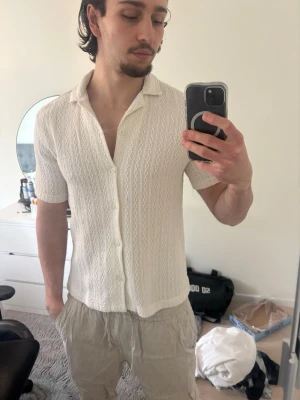 Vit kortärmad skjorta med mönster - Säljer en vit skjorta med korta ärmar och diskret mönster. Skjortan har knappar framtill och en avslappnad krage. Perfekt för dig som gillar en clean och stilren look med lite extra detalj i tyget.