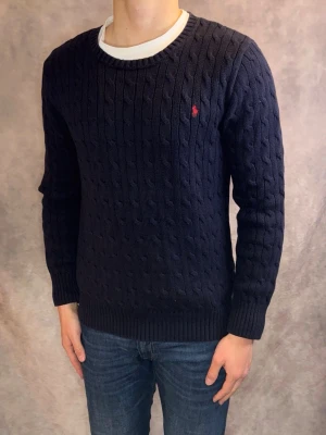 Kabelstickad Ralph Lauren Tröja - Stl Xl (18-20) / S - Riktigt snygg Kabelstickad Ralph Lauren tröja i färgen marinblå | Mycket bra skick: 8,5/10, lätt urtvättad men inga defekter | Stl: S/ Xl (18-20) som är en barnstorlek som passar Herr S, modellen är 177cm och väger 75kg, passar dig bäst vid ca 168-175cm | Nypris: Ca 1800kr | Hör av dig vid frågor // Galgen 🫡