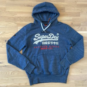 Blå Superdry hoodie  - Säljer en riktigt schyst superdry hoodie i storlek L. Den är i toppskick och har knappast några tecken på användning. 