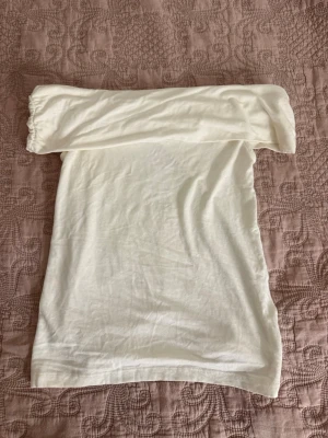 Vit axelbandslös tubtopp - Snygg vit axelbandslös tubtopp i mjukt material. Perfekt att styla med jeans eller kjol för en clean och enkel look. Toppen har en bandeau-form och är stretchig för en bekväm passform.