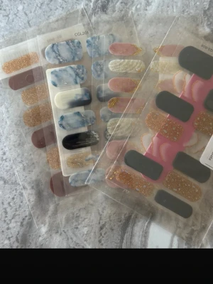 Nagelstickers i mixade färger och mönster - Säljer flera ark nagelstickers i olika färger och mönster. Innehåller bland annat glitterguld, vinrött, marmorerat blått och vitt, svart samt rosa med gulddetaljer. Perfekt för dig som vill fixa snygga naglar snabbt och enkelt hemma. Självhäftande och enkla att applicera.