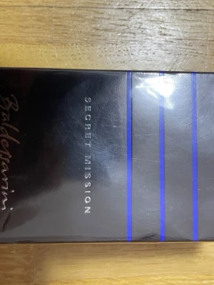 Baldessarini Secret Mission parfym - Baldessarini Secret Mission parfym i en elegant svart förpackning med blå linjer och silvertext. Förpackningen har en modern och stilren design som känns lyxig och maskulin. Perfekt för dig som gillar exklusiva dofter och vill ha något unikt i badrumsskåpet.