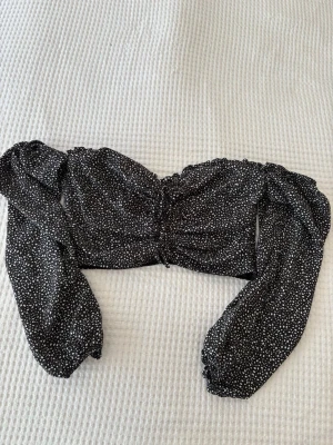 Cropp topp - Trendig svart croppad blus med vita prickar och långa puffärmar. Toppen har en söt rynkad detalj framtill och resår vid ärmslut. Perfekt för dig som gillar en feminin och cool stil.