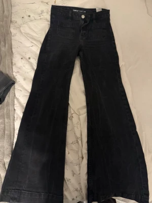 Svarta utsvängda jeans - Säljer ett par svarta utsvängda jeans från Camille med hög midja och raka fickor framtill. Jeansen har en snygg tvättad look och vida ben som ger en retrovibe. Perfekta för dig som vill ha en trendig och bekväm stil. Från bikbok storlek: midja 27 längd 30. De är svarta men blivit lite gråa i tvätten och fått lite ränder.