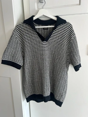 Randig stickad tröja med V-ringning - Säljer en snygg stickad tröja med kort ärm och V-ringning. Tröjan har marinblå och vita ränder, bred ribbad kant i halsen, ärmslut och nederkant. Perfekt till jeans eller kjol för en avslappnad look.