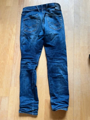 Mörkblå slimmade replay jeans  - Säljer ett par mörkblå jeans från Replay med raka ben och klassisk femficksdesign. Jeansen har snygga slitningar och kontrastsömmar, samt bälteshällor och knappgylf. Perfekta för en avslappnad och trendig look. Kan vara lite slimmade.