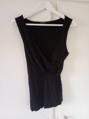 Svart omlottopp från La Redoute - Snygg svart omlottopp från La Redoute Création med djup v-ringning och ärmlös design. Perfekt att styla med jeans eller kjol för en trendig look. Tunn och mjuk i materialet för en bekväm känsla.