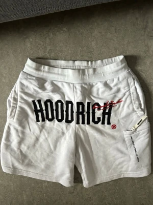 Vita HOODRICH shorts - Ett par Vita Hoodrich shorts med röda och svarta siffror. Perfekt till sommaren, väldigt sköna och är perfekt för din storlek. Storlek S men XS och M kan använda de också. SHORTSEN ÄR 100% Äkta