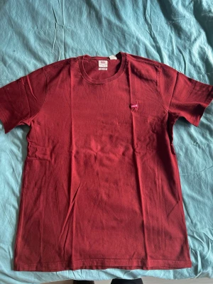 Röd Levi's t-shirt i bomull - Snygg röd t-shirt från Levi's med klassisk passform och liten logotyp på bröstet. Tillverkad i mjuk bomull och har rund halsringning samt korta ärmar. Perfekt till jeans eller shorts för en enkel och stilren look.