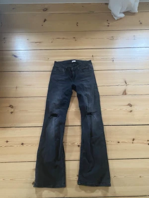 Svarta bootcut jeans med hål - Säljer ett par svarta bootcut jeans med hål på båda knäna. Detaljer på fickorna. 