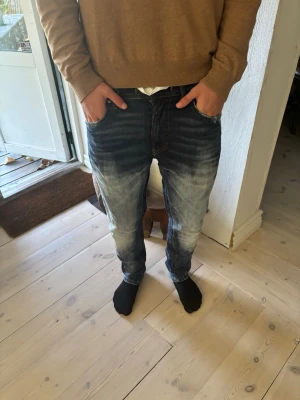 Blåa Disel jeans med slitningar - Säljer ett par blåa Disel jeans med tvättade detaljer samt snygga slitningar på både bak och framsidan. Jeansen har en slim passform tillsamans med 5 fickor.