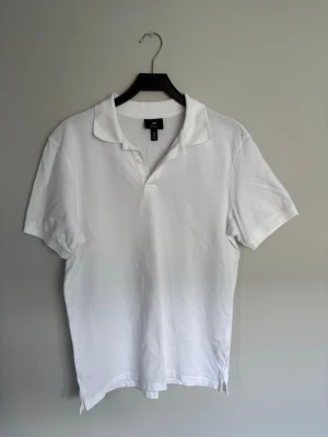 Vit pikétröja från H&M, regular fit - Klassisk vit pikétröja från H&M i regular fit. Tröjan har korta ärmar, krage och knappar vid halsen. Tillverkad i mjuk bomull som känns skön mot huden. Perfekt till jeans eller shorts för en clean och enkel stil.