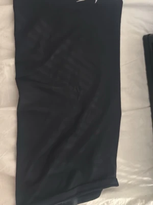 Svarta mask från Nike - Säljer en svart mask från Nike med den klassiska vita swoosh-loggan framtill. Den är stretchig. Materialet känns mjukt och följsamt mot kroppen.