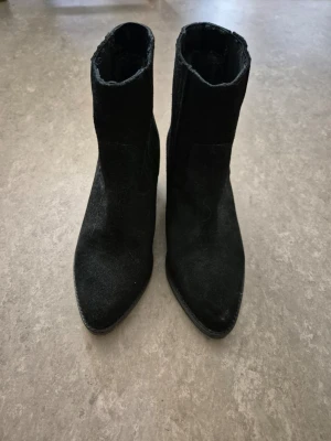 Boots - Snygga svarta stövletter i mocka med spetsig tå och medelhög klack. Klassisk och stilren modell som passar till många outfits. Materialet är mjukt och ger en lyxig känsla. Perfekta för dig som gillar en trendig och tidlös look.
