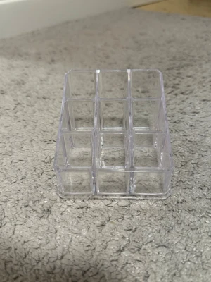 Transparent sminkorganiserare i plast - Praktisk och stilren sminkorganiserare i transparent plast med nio fack. Perfekt för att hålla ordning på sminkborstar, pennor eller andra små skönhetsverktyg. Den rektangulära formen gör den enkel att placera på sminkbordet.