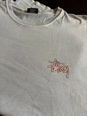 Ljusblå Stüssy t-shirt med logga - Ljusblå t-shirt från Stüssy med klassisk logga i rosa på bröstet. tillverkad i bomull. Från 2000 tal. Fin blå färg men svårt att få på bild! Inga side seems så fin passform! 