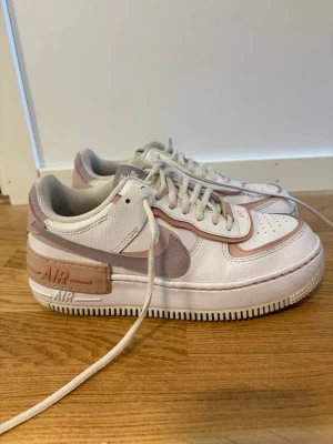 Nike Air Force 1 vit/rosa - Nike Air Force 1 Shadow sneakers i vitt och ljusrosa med detaljer i beige och lila. 