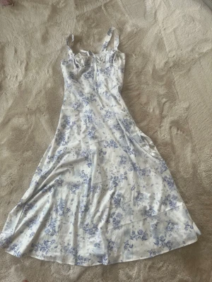 Blommig vit och blå klänning Carmen - Romantisk långklänning från  i vit med blått blommönster. Klänningen har smala axelband, markerad byst med snörning framtill och en vacker, utsvängd siluett. Perfekt för sommarens alla tillfällen. Den är storlek M men om man drar in midjan med säkerhets nål eller likande så har den passat xs-s.  . Säg till om du vill diskutera pris. 💕