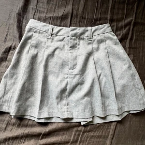 Grå skort med vida ben - Stilren grå skort med vida ben och klassiska pressveck. Har hällor för skärp och dold dragkedja fram. Materialet är mjukt och ser ut som en blandning av bomull och polyester. Perfekt för en trendig och avslappnad look.