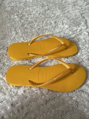 Gula flip-flops från Havaianas - Snygga gula flip-flops från Havaianas med klassisk design och tunna remmar. Tillverkade i mjukt och flexibelt gummi som är perfekt för sommaren. Märkets logga syns på remmen och sulan har en strukturerad yta för extra grepp.