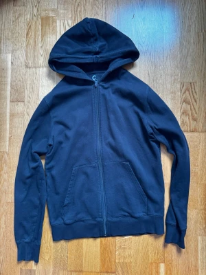 Mörkblå zip hoodie med fickor - En enkel och stilren mörkblå hoodie från Gildan med dragkedja framtill och två stora fickor. Hoodien har en klassisk huva och ribbade muddar vid ärmslut och nederkant. Perfekt för en avslappnad look och passar till det mesta.