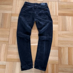 Svarta nudie jeans - Säljer ett par svarta nudie jeans i storlek W30/L32. Modellen är steady Eddie. Byxorna är använda och har lite tecken på användning t.ex lite slitningar längst ner på benen (se bild7). Men inget som syns särskilt mycket vid användning. Hör av er vid frågor :)