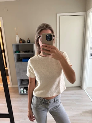 Beige croppad topp i bouclé - Säljer en beige croppad topp i bouclé-liknande material. Toppen har korta ärmar och en boxig passform med tre guldknappar på ena axeln. Kom aldrig till användning.