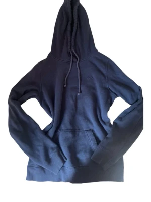 Mörkblå hoodie med huva - En stilren mörkblå hoodie med stor huva och dragsnören. Klassisk känguruficka framtill och ribbade muddar vid ärmar och nederkant. Perfekt för en avslappnad look och enkel att matcha med jeans eller mjukisbyxor.passar för bege killar och tjejer, är kille och använde den men är nog även för tjejer
