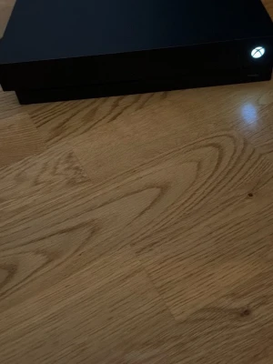 Xbox One X spelkonsol svart - Säljer en svart Xbox One X spelkonsol från Microsoft. Konsolen har en stilren, rektangulär design med mattsvart finish och tydlig Xbox-logga på framsidan. Perfekt för gaming och streaming i hög kvalitet. 