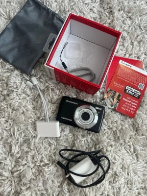 digitalkamera svart - Säljer en svart digitalkamera från Agfaphoto med 16 megapixlar och stor display på baksidan. Kameran har silverfärgade detaljer runt linsen och knapparna. Medföljer originalkartong, handledsrem, laddkabel, adapter och förvaringspåse. 