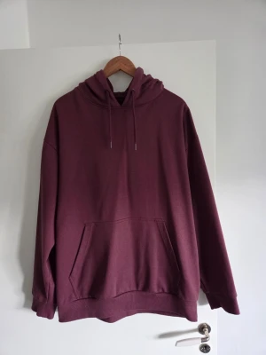 Vinröd hoodie från 157 - Säljer en vinröd hoodie från Lager 157 i storlek L. Hoodien har en klassisk känguruficka framtill och ribbade muddar vid ärmslut och nederkant. Perfekt för en avslappnad och stilren look.