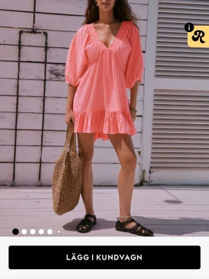 Kort rosa klänning med volang - Söt kort klänning i ljusrosa med v-ringning och volangkant nedtill. Klänningen har trekvartsärmar med lätt puff och avslappnad passform. Perfekt för varma dagar och enkel att styla med sandaler eller sneakers. Endast provad och lappen finns kvar!