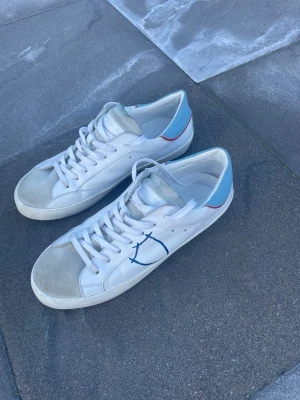 Philippe model skor  - Tjabba!! Säljer ett par vita sneakers från philippe model med blå häl och röd rand baktill. Skorna har en blå ”målat” märke (det är fabrik målat så de ska va så) på sidan och vita skosnören. Ovandelen är i läder med mockadetaljer på tån. Klassisk låg modell som passar till det mesta. Perfekta skor nu när sommaren och värmen är kommen!! Skick 9,5/10 storlek 39 kan kanske passa 40!! Pris endast 799kr!! Hör av dig vid mer frågor eller funderingar😁mvh Ga🕺🤩