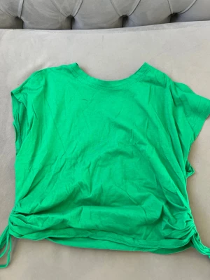 Grön topp med snörning från Zara - Snygg grön topp från Zara i mjuk bomull. Modellen är ärmlös med rund halsringning och har cool snörningsdetalj i sidorna som ger en trendig look. Perfekt att styla till jeans eller kjol för en fräsch vibe.