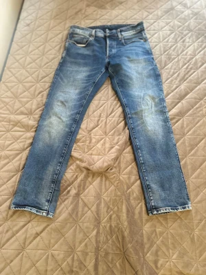 Blå raka jeans med slitningar - Säljer ett par klassiska blå jeans med raka ben och snygga slitningar på låren och knäna. Jeansen har fem fickor, normal midja och är gjorda i denim med kontrastsömmar. Perfekta för en avslappnad och trendig look.