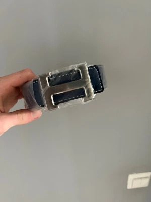 Mörkblått skärp med stor H-spänne - Mörkblått läderbälte som passar till alla kläder. Skickas oftast samma dag eller dagen efter.