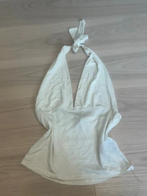 Vit halterneck linnetopp - Snygg vit halterneck topp med knyt i nacken och djup v-ringning. Toppen är ärmlös och har en croppad passform som ger en trendig look. Tillverkad i mjukt bomullsmaterial som känns skönt mot huden. , har en svart prick som inte går bort, o någon defekt på magen. 