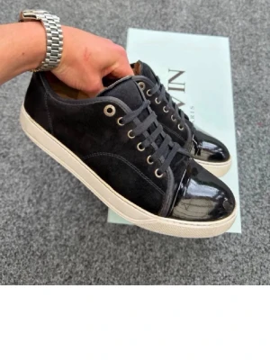 Svarta lanvins - Snygga svarta sneakers från Nalin med ovandel i mocka och glansiga lackdetaljer på tån och hälen. Skorna har vita sulor, svarta skosnören och metallfärgade öljetter. Perfekta för en trendig och stilren look. Hör av er vid minsta lilla fråga