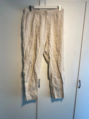 H&M Beiga linnebyxor - Säljer ett par beiga H&M linnebyxor med avslappnad passform och resår i midjan. Byxorna har raka ben och sidofickor, perfekta för en chill och stilren look. Tillverkade i svalt linnematerial som passar grymt under varmare dagar.