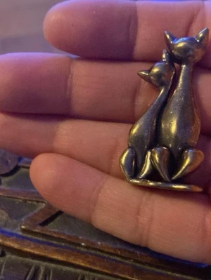 Vintage retro figur figurin med två katter i mässing -  i mässing med två stiliserade katter som sitter tätt ihop. Designen är elegant och retro, perfekt för dig som gillar djurmotiv och vill ha en personlig accessoar.  har en varm guldfärgad ton och passar snyggt 