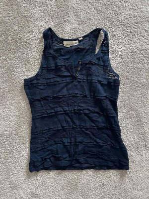 Mörkblå spetslinnetopp med knappar - Supersnygg mörkblå linnetopp från h&m med spetsdetaljer och dekorativa knappar framtill. Toppen är ärmlös och har ett figurnära snitt med transparenta spetsränder som ger en cool och feminin look. Perfekt att styla till jeans eller kjol.💗💗