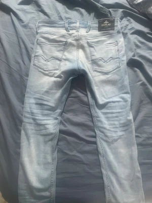 Ljusblå Replay Anbass - Säljer ett par ljusblå skinny jeans från Replay med klassisk femficksdesign och snygga slitningar. Jeansen har raka ben, normal midja och är tillverkade i mjuk denim med stretch för extra komfort. Perfekta för en avslappnad och trendig look. Litet hål vid skrevet (se sista bild) W31, L32